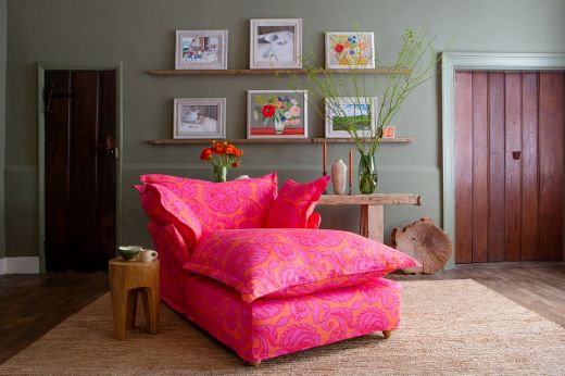 Maker and Son cosy comfy chaise longue upholstered in Anna floral fabric with pink and orange hues, set in a green-painted room.