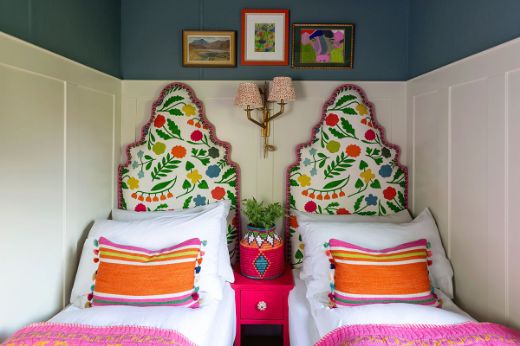 Children's bedroom with two single beds featuring Array Linen Floral Fabric green multi-coloured headboards, set in a fresh, fun, and whimsical interior with white panelling, navy blue walls, and pink and orange accessories. Design by Jo Bee.