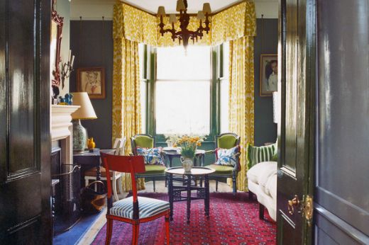 Classic eclectic English drawing room interior with Belfour Damask lemon yellow curtains with a pelmet, green chairs, and a red rug. Photography by James Mcdonald