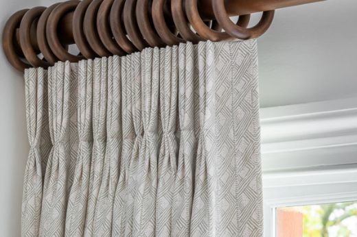 Triple pinch pleated curtains in Belge Neutral-colored geometric and soft pink dotted linen fabric, hanging on a wooden pole, designed by Otta Design. Photography by Jonathan Bond.