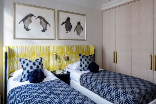 Guest bedroom designed by Gunter & Co Interiors, featuring Breakwater linen fabric in lemon yellow on a headboard across two single beds, with blue bedding and accessories, and penguin pictures on the wall.