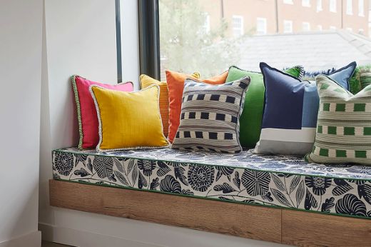 Cushions in bright soprano colours, alongside some cushions in Christopher Farrs lost and found fabric. All sat in a window seat made out of Christopher Farrs Eden fabric in a navy.