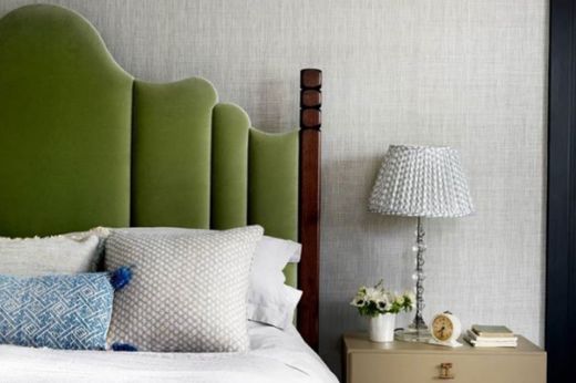 Bedroom featuring textured Birch Raffia wallpaper in slate grey, complemented by a green velvet scalloped-shaped headboard. The sophisticated interior blends traditional and modern design with blue and grey cushions, and a matching lampshade, creating an elegant, cosy atmosphere.