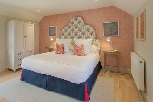 Classic hotel bedroom featuring a large superking bed with a navy valance and navy bouquet fabric headboard. The walls are covered in a custom red colourway of Bulu Raffia Wallpaper, adding rich texture and warmth to the luxurious, timeless interior.