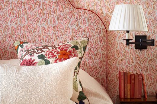 A bedroom featuring an upholstered headboard crafted from Armatures Feuilles luxury printed linen fabric with a hot pink and orange leaf design, paired with matching wallpaper in the same vibrant colourway. Designed by Yellow London, with photography by Matt Clayton.