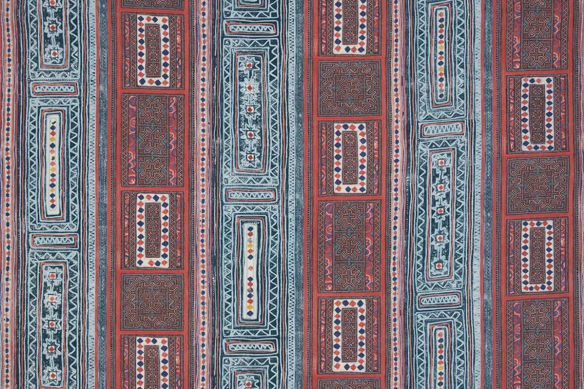 A vibrant textile with vertical stripes and geometric patterns featuring diamonds, florals, and intricate borders in red, blue, white, and yellow.