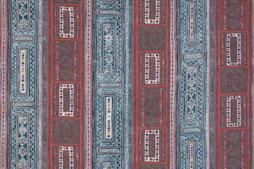 A vibrant textile with vertical stripes and geometric patterns featuring diamonds, florals, and intricate borders in red, blue, white, and yellow.