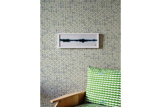 Interior room with green fish wallpaper, a framed print, and a green wave-patterned cushion on a wooden chair. Photography by Christopher  Horwood